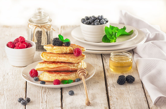 Delicious ready-made golden pancakes with fresh blueberries, raspberries and honey