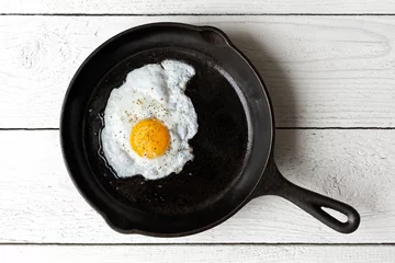 Fotobehang Spiegeleieren Single fried egg in cast iron frying pan sprinkled with ground black pepper. Isolated on white painted wood from above.