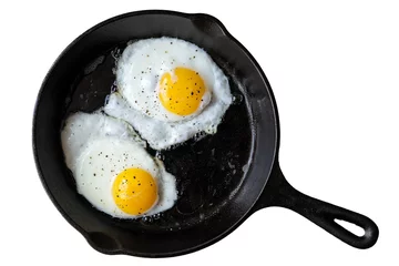 Keuken foto achterwand Spiegeleieren Twee gebakken eieren in gietijzeren koekenpan bestrooid met gemalen zwarte peper. Geïsoleerd op wit van bovenaf.