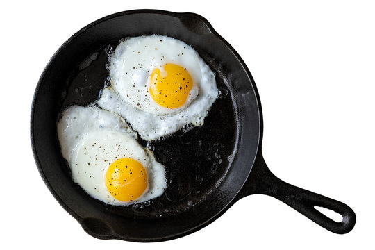 Two fried eggs in cast iron frying pan sprinkled with ground black pepper. Isolated on white from above.