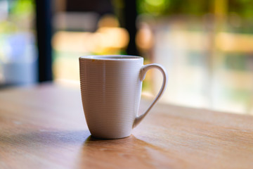 White coffee or tea mug on a wooden desk next to a window