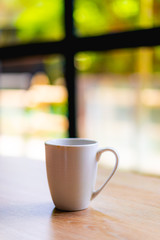 White coffee or tea mug on a wooden desk next to a window