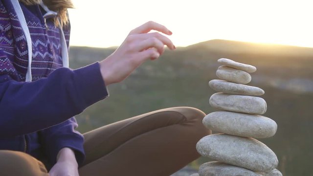 Girl collects a pyramid of stones close up at sunset