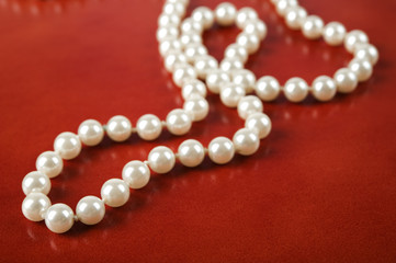 White pearl necklace on red leather background.