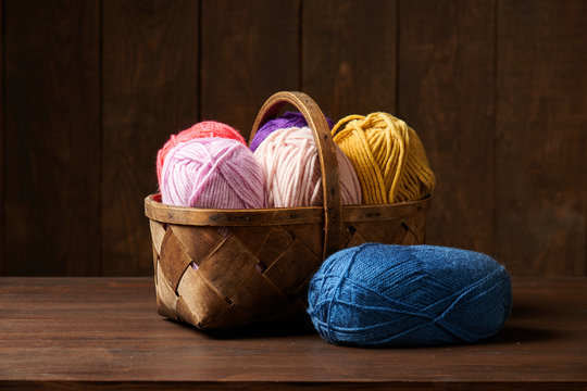 colorful wool yarn for knitting in basket, wooden background
