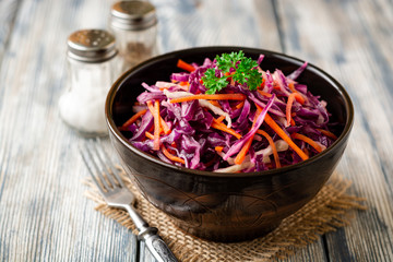 Fresh coleslaw salad with red and white cabbage and carrots in bowl on vintage wooden background. Selective focus.