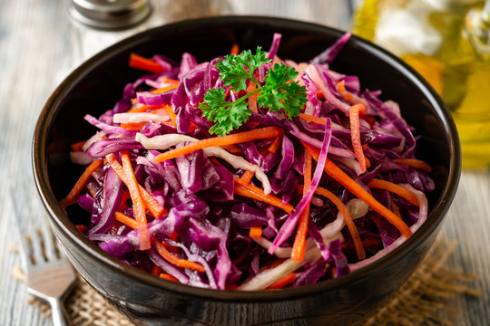 Fresh coleslaw salad with red and white cabbage and carrots in bowl on vintage wooden background. Selective focus.