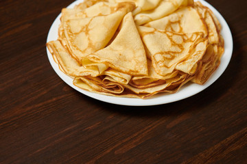 Crepe closeup, heap of thin pancakes on a dish, wood background