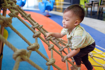 Cute little Asian 2 years old toddler baby boy child having fun trying to climb on jungle gym at...