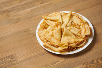 Crepe closeup, heap of thin pancakes on a dish, wood background