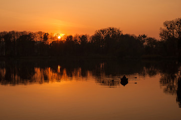 Young couple in a boat sailing on a lake at sunset. Silhouettes of romantic couple sailing in a boat against the backdrop of the orange sunset.