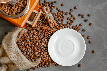 Cup of coffee with steam, coffee beans, chocolate pieces, cinnamon sticks, white and brown sugar, and scoop on burlap background.