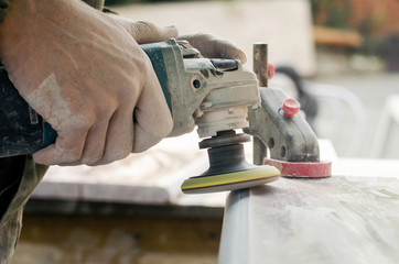 A man polishing a gray marble stone with a small angle grinder. working man the creation of monuments