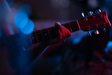 Naklejka premium Woman's Hand Plays Guitar Chord in Stage Lighting