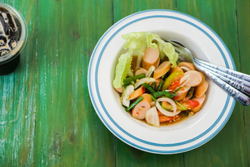 Sausage spicy salad in a bowl put on the green table.