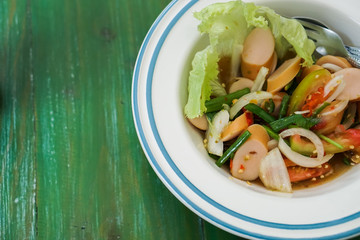 Sausage spicy salad in a bowl put on the green table.