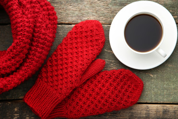 Knitted red gloves and scarf with cup of coffee on wooden table