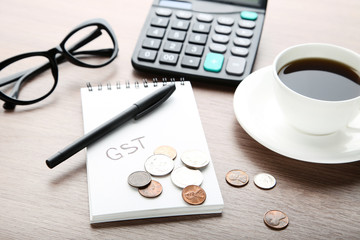 Inscription GST on paper with coins, calculator, glasses and cup of coffee