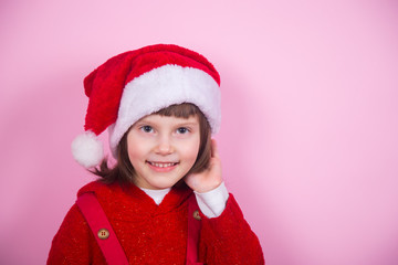 Cute smiling little girl in Santa hat and Christmas costume in studio on pink background.
