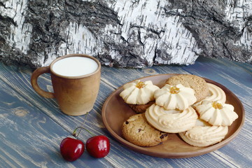 Obraz na płótnie Canvas Dessert. A mug of milk and a delicious shortbread cookie on a clay plate. Wooden table top and birch bark in the background.