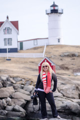 Beautiful blonde woman photographer poses in front of Portland Head Lighthouse in Portland Maine is one of Maine's most famous historical landmarks