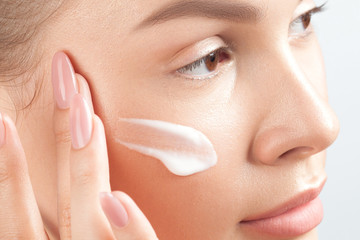 Young beautiful woman applies cream on clean perfect skin
