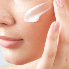 Young beautiful woman applies cream on clean perfect skin