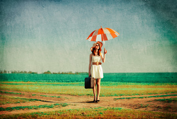 Redhead girl with umbrella and suitcase at spring countryside.