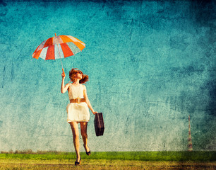 girl with umbrella and suitcase jumping over road at spring season countryside.