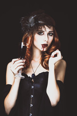 Obraz premium Redhead vampire woman with glass of blood. Photo in vintage style.