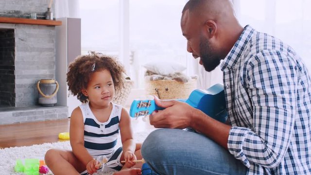 Young black dad playing ukulele and singing to his daugther