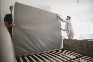 Couple Setting Up Bed Together in New Home - obrazy, fototapety, plakaty