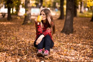 Young woman drink hot tea in autumn park
