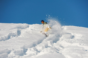 Snowboarder in bright sportswear riding down a snow hill on bright sunny winter day