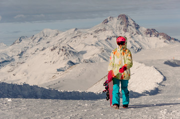 Woman snowboarder in pink sports helmet and bright colorful sportswear against the mountains peaks