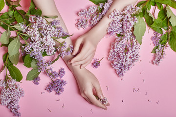 Fashion art hands natural cosmetics women, bright purple lilac flowers in hand with bright contrast makeup, hand care. Creative beauty photo of a girl sitting at table on contrasting pink background