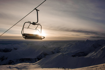Cable car cabin hanging on the background of high mountain peaks and sky with shining sky