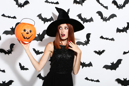 Beautiful redhaired woman with pumpkin bucket and paper bats on white background