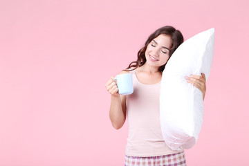 Beautiful girl holding cup of tea and white pillow on pink background