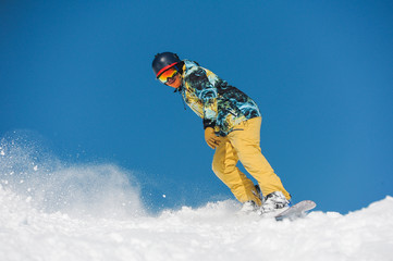 Young active snowboarder in bright sportswear riding down a mountain slope