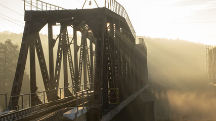 A railway bridge in the morning fog or smoke through which the rays of the sun shine
