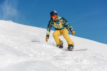 Fototapeta na wymiar Snowboarder in bright sportswear riding down a mountain slope