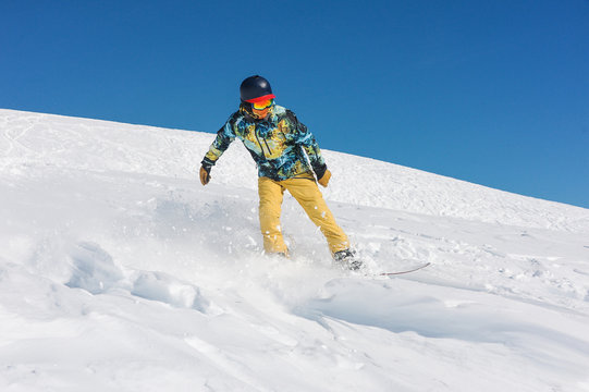 Professional man snowboarder in bright sportswear riding down a mountain slope