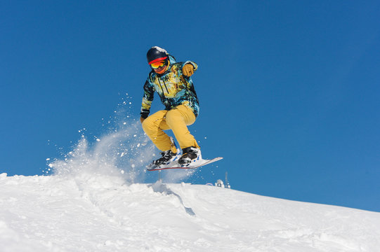 Young active snowboarder in bright sportswear jumping up on a mountain slope