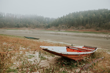 Anchored abandoned old fishing red boat on the bank of the empty Orl&iacute;k Reservoir in foggy autumn day