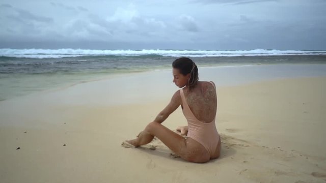 Brunette woman in sweemware posing seatting on sendy beach in cloudy wether