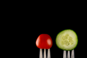 Tomato and cucumber on fork on black background, copy space