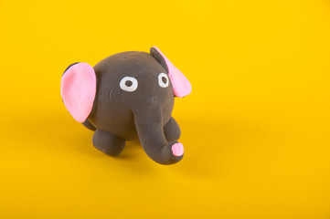 Funny elephant made of modelling dough staying on yellow background