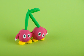 Funny toy cherries with hands and eyes staying on green background
