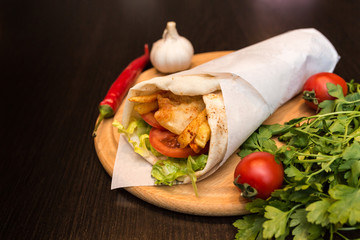 Shawarma sandwich giros - fresh roll of thin lavash (pita bread) filled with grilled meat, mushrooms, cheese, cabbage, carrots, sauce, green. Traditional Eastern snack. On a wooden background